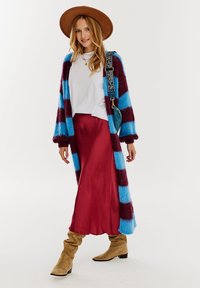 Wielokolorowy kardigan w niebieskie i burgundowe paski, nałożony na biały top i burgundową satynową spódnicę. Dodatki to brązowy kapelusz i torebka.