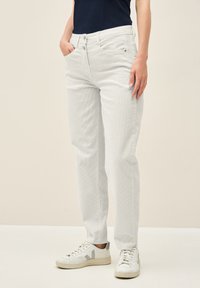 Pantalones de corduroy gris claro con corte recto, que cuentan con bolsillos frontales y cremallera, combinados con zapatillas blancas.