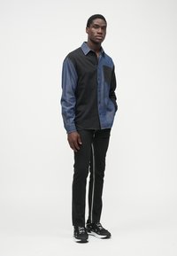 Cămașă cu nasturi, cu panouri de culoare bleumarin închis și negru, având un buzunar pe piept. Combinată cu pantaloni negri slim și adidași negri.