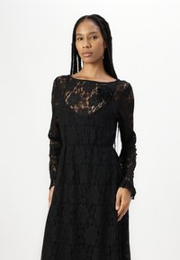 Μαύρο δαντελένιο φόρεμα με μακριά μανίκια, ανθιστόλη σχέδιο και στρογγυλή λαιμόκοψη. Διαθέτει διακοσμητική ανθοκομία στην περιοχή του στήθους.