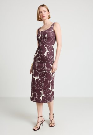 Donna che indossa un abito midi senza maniche con grandi motivi floreali viola scuro su sfondo chiaro, abbinato a sandali alti scuri con cinturini.