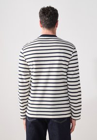 Kermanhoushuva cream colored shirt with navy stripes, featuring a rounded neckline and a relaxed fit, viewed from the back. Soft fabric texture, casual style.