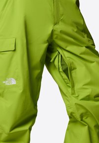 Limegröna vattentäta byxor med en slät yta, med blixtlåsförsedda ventiler och den vita "The North Face"-logotypen på sidan.