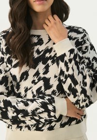 Czarno-biały sweatshirt w wzory z prążkowanym dekoltem i mankietami, o luźnym kroju i miękkiej teksturze materiału.