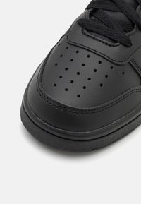 Schwarze Sneaker mit Obermaterial aus glattem Leder, durchbrochenem Design an der Zehenpartie, strukturiertem Gummisohle und flachen schwarzen Schnürsenkeln.