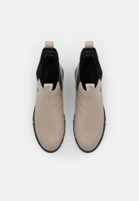 Bottines en cuir beige avec un panneau élastique noir, bout arrondi et semelle en caoutchouc texturé. Elles sont dotées d'une languette pour un enfilage facile.