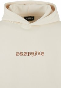 Beige Kapuzenpullover mit einem großen braunen gestickten "DROPSIZE"-Logo auf der Vorderseite. Weicher Stoff mit Kapuze zum Verstellen und lockerer Passform.