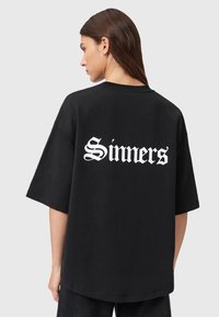 Zwart oversized t-shirt van katoen met korte mouwen. De achterkant heeft gedurfde witte gotische letters met de tekst "Sinners."