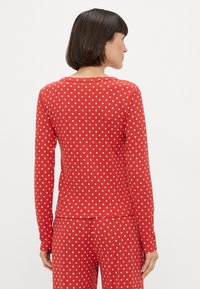 Czerwona bluzka z długim rękawem w białe kropki, z okrągłym dekoltem i dopasowanym krojem. Teksturowany materiał współgra z pasującymi spodniami.