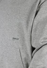 Grauer Sweatshirt aus weichem Material mit einer Kängurutasche und einem schwarzen "SIKSILK" Logo mit "Est 2012" darunter, auf der Brust platziert.