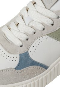 White leather sneaker with grey and blue suede accents, textured surface, thick white laces, and perforated detailing near the toe.