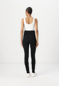 Zwarte hoge taille leggings met een geplooid achterontwerp, gecombineerd met een witte tanktop. Glad stoffen textuur; enkellange pasvorm en minimalistische stijl.