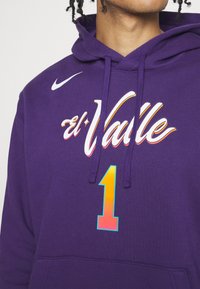 Sweat à capuche violet avec un motif à l'avant comprenant "el Valle" en lettres blanches et orange et un grand "1" dégradé en dessous. Logo Nike sur l'épaule gauche.