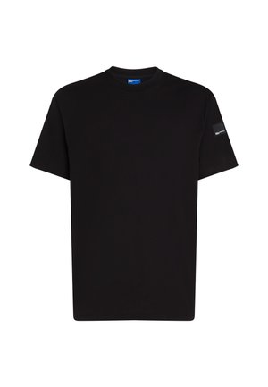 T-shirt en coton noir à manches courtes, décolleté rond, avec une petite étiquette accentuée sur la manche gauche. Texture lisse, coupe standard.