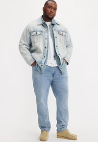Svetla denim jakna, usklajena majica, bela majica, svetlo modri kavbojki in bež obutev. Ima klasične žepe in gumbne detajle.