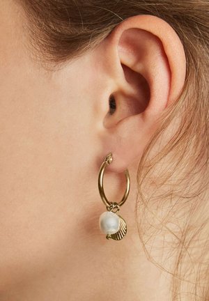 Pendiente de aro dorado con una perla blanca y un pequeño acento de concha, mostrado en una oreja. El pendiente tiene un acabado brillante y suave.