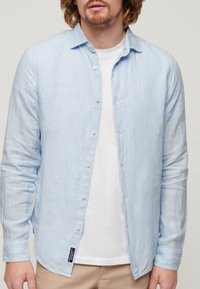 Lichtblauw gestreept overhemd met lange mouwen en een button-down kraag, witte knopen en een klein label aan de zoom. Draagt een wit T-shirt eronder.