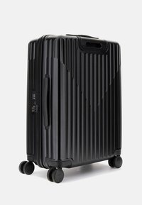 Valigia rigida nera con texture a righe verticali, dotata di maniglia superiore, doppie ruote e lucchetto combinato per la sicurezza.