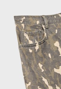 Close-up van camouflage-gedessineerde denim jeans met een voorzak en een riemlus op een lichte achtergrond.