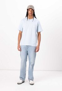 Light blue cotton t-shirt with short sleeves, paired with light blue jeans. Accessorized with a gray cap and white sneakers with gray accents.