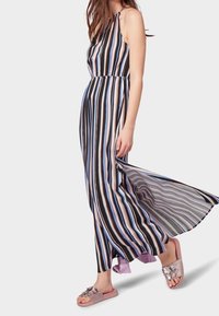 Vestido maxi con rayas verticales en negro, azul y rosa; diseño de halter. Tejido fluido. Lleva unos zapatos de lona morados claros con adornos.