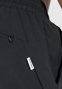 Pantalones cortos deportivos negros hechos de un tejido ligero, con una cintura elástica, bolsillo con cremallera y una etiqueta blanca con la marca "SMILODOX".