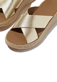 Gouden faux leren wedge sandalen met gekruiste banden en gevlochten jute zool. Heeft een bruine voetbed, een gladde textuur en een strak ontwerp.