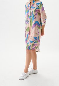 Abito con stampa floreale colorata, caratterizzato da un colletto oversize, una chiusura frontale con bottoni e maniche a tre quarti, realizzato in tessuto leggero. Indossato con sneakers bianche.
