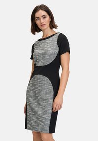 Schwarzes Kleid mit kurzen Ärmeln, das ein strukturiertes graues Panel über der Brust und eine größere graue Akzentuierung an der unteren Seite aufweist.