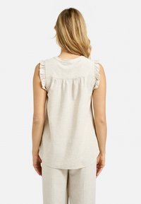 Beige Leinen-Top ohne Ärmel mit Rüschendetails an den Schultern, gesammeltem Design am Rücken und glatter Textur, kombiniert mit einer passenden Hose.