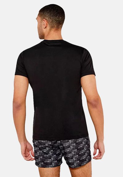 T-shirt noir à manches courtes avec un col rond, au design ajusté, présenté de dos. Porté avec un short noir à motifs comportant du texte.