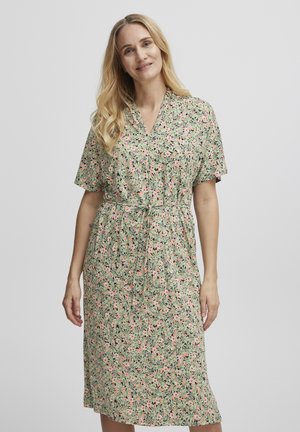 Blommig klänning med grön bas och mönster i rosa och svart, korta ärmar, V-ringning och en cinchad midja med detaljerad knytning.