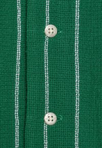 Grön texturerad duk med vita vertikala ränder, prydd med en silverknapp med präglingen "JACK & JONES" och fyra knapphål.