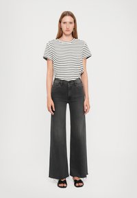Striped black and white t-shirt, high-waisted dark denim flared jeans, and black sandals. Casual outfit with classic patterns and textures.