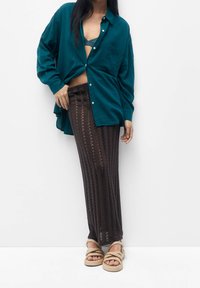 Chemise oversize boutonnée bleu sarcelle, jupe en crochet marron avec motifs verticaux, et sandales tressées couleur tan. Tissu lisse avec accents texturés.