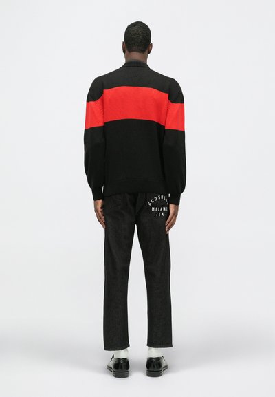 Suéter tricotado preto e vermelho com um padrão de riscas horizontais, combinado com calças de denim escuras que apresentam um logótipo gráfico na parte de trás.