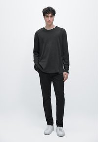 Langärmeliges, dunkelgraues Baumwollhemd in Kombination mit schwarzer Hose und weißen Turnschuhen, mit lockerer Passform und Rundhalsausschnitt.