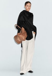 Wrap in lana nera, veste ampia. Pantaloni bianchi a gamba larga. Borsa in pelle marrone con hardware e texture visibili. Design liscio e minimalista.