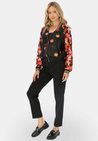Czarna kurtka bomberka z kwiatowym wzorem na rękawach, z ribbowanym dołem, w połączeniu z dopasowanymi czarnymi spodniami i błyszczącymi czarnymi loafersami.