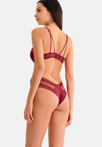 Ensemble de lingerie bordeaux comprenant un bralette avec des bretelles fines et réglables, accompagné d'un string assorti avec des accents en dentelle et des panneaux en mesh.