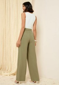 Lichtgroene wijde broek met een elastische tailleband, gecombineerd met een aansluitend wit mouwloos topje. Glad oppervlak en strakke lijnen.