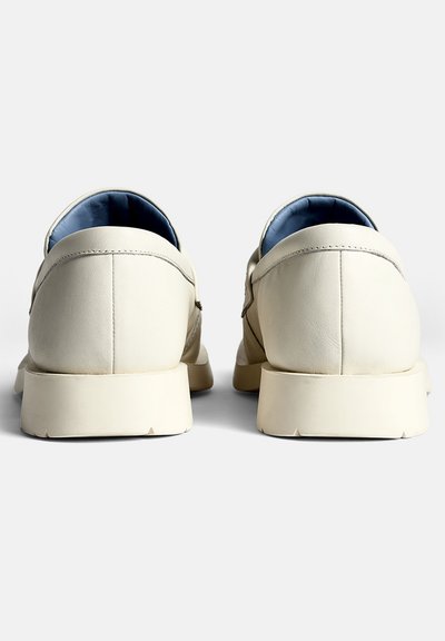 Cream leather shoes with a smooth texture, rounded shape, and a minimalist design. Blue lining and cushioned sole visible from the back.