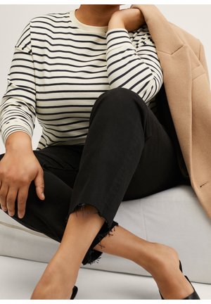 Haut à manches longues rayé crème et marine, associé à un jean noir effiloché. Un blazer beige est porté au bras. Design simple aux lignes épurées.