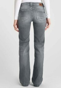 Jean en denim gris évasés avec une taille mi-haute, des poches arrière et une étiquette en cuir marron au niveau de la ceinture. La texture est légèrement usée.