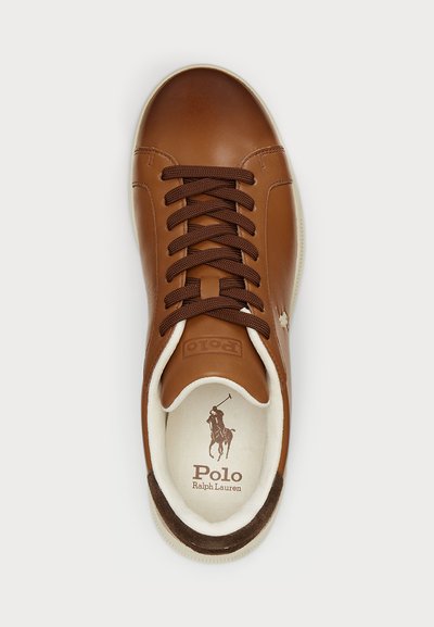 Rjavi usnjeni superge s temno rjavimi vezalkami, belim obrobom in oblazinjeno podplatom s logotipom. Gladka površina z minimalnimi podrobnostmi.