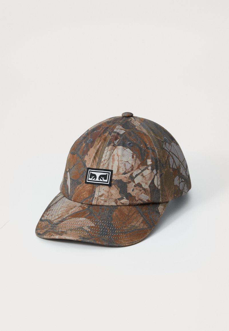 Woodland camouflaged baseball cap i nuancer af brunt, gråt og crème; har en rund krone, buet skygge og et sort logo-patch.