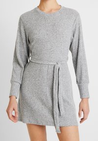 Harmaa ribattua mekkoa pitkillä hihoilla ja vyöllä, pehmeästä neulostuotteesta valmistettu, jossa on pyöreä pääntie ja hillitty pinta.