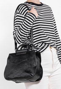 Mustassa nahkalaukussa on rakenteellinen muotoilu, lyhyt kahva ja pitkä säädettävä olkahihna. Sen pinta on sileä ja design minimalistinen.