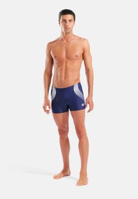 Μπλε ναυτικό μαγιό βερμούδα με εφαρμοστό σχέδιο, διαθέτει λευκές διχτυωτές λεπτομέρειες στις πλευρές, κατασκευασμένο από ελαστικό υλικό, κατάλληλο για κολυμβητικές δραστηριότητες.