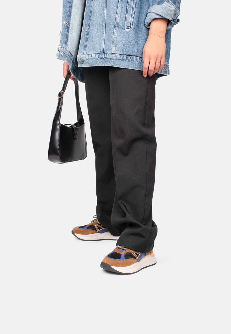 Mehrfarbige Sneakers aus Wildleder und Mesh-Materialien, mit blauen, braunen und schwarzen Akzenten. Kombiniert mit schwarzen Hosen und einer Jeansjacke.